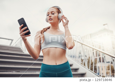 Woman, runner and phone with headphones for music, radio and web texting on chat app by stairs. Gen z girl, urban workout and fitness with smartphone for networking, social media and internet in city 129718646