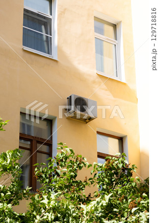 air conditioner on wall of an apartment building with view of green trees. air conditioner on wall of an apartment building with view of green trees. 129718816