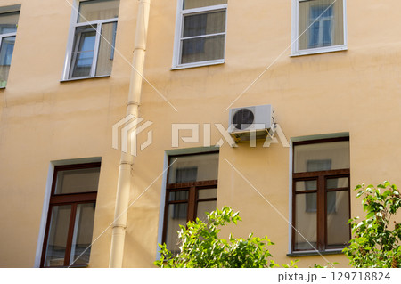 air conditioner on wall of an apartment building with view of green trees.  129718824