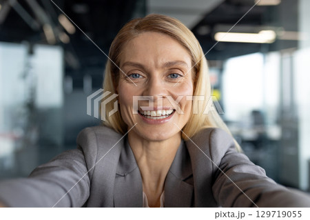 Confident professional woman smiling and taking a selfie in a modern office environment. Capturing an empowering moment reflecting positivity and professionalism. 129719055