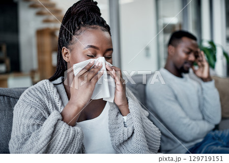Young, sick and ill woman blowing her nose with tissues while sitting on the couch at home. African lady has cold or flu and needs medicine. Husband worried about wife suffering from illness 129719151