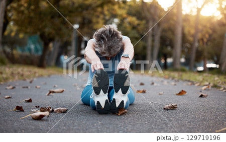 Woman, fitness and stretching exercise while sitting on asphalt road with autumn leaves for exercise, workout and warm up at nature park. Female on group for energy, health and wellness touching feet 129719196