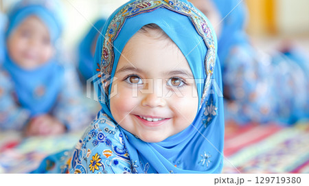 Young girl wearing blue hijab smiles brightly in colorful traditional attire with joyful ambiance Young girl wearing blue hijab smiles brightly in colorful traditional attire with joyful ambiance 129719380