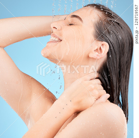 Happy woman, shower and water drops in studio blue for healthy glow, shine and cosmetics cleaning in bathroom with side profile. Excited, calm and facial beauty model in water splash for dermatology 129719567
