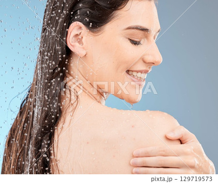 Water, body shower and happy woman on studio blue background for healthy skincare, beauty and personal hygiene. Young model, water splash and washing for wellness, cosmetics and cleaning in bathroom 129719573