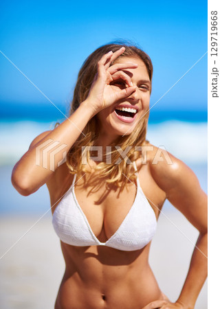 Summer, smile and bikini with woman at beach for travel destination, relax and vacation in the Maldives with okay sign. Happy, sexy and tropical with girl on overseas adventure for holiday trip 129719668