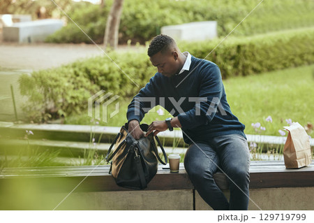 Businessman city park, food and lunch break with coffee or tea drink in paperbag. Young African entrepreneur looking in bag for strategy notebook and sitting outside in urban environment alone Businessman city park, food and lunch break with coffee or tea drink in paperbag. Young African entrepreneur looking in bag for strategy notebook and sitting outside in urban environment alone 129719799