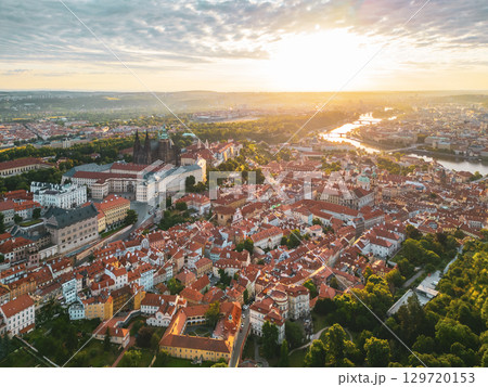 Golden sunlight bathes Prague Castle and its surroundings at dawn, casting long shadows across the red rooftops of the historic city. A moment of tranquility before a busy day begins. 129720153