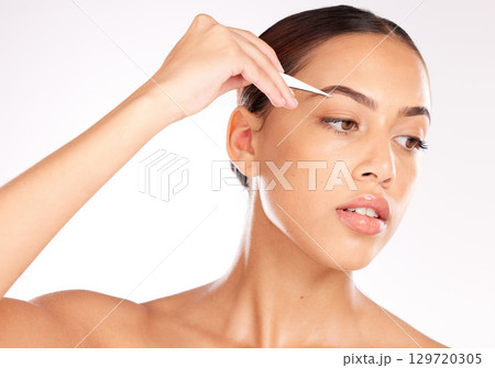 Hair removal, model or woman with a tweezer for eyebrow beauty, skincare or grooming in studio on white background. Wellness, face and young relaxed girl plucking eyebrows in a self care routine Hair removal, model or woman with a tweezer for eyebrow beauty, skincare or grooming in studio on white background. Wellness, face and young relaxed girl plucking eyebrows in a self care routine 129720305