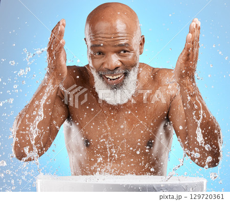 Water splash, senior and black man cleaning face in studio isolated on a blue background. Skincare, hygiene and retired elderly male from Nigeria bathing or washing for wellness and healthy skin. Water splash, senior and black man cleaning face in studio isolated on a blue background. Skincare, hygiene and retired elderly male from Nigeria bathing or washing for wellness and healthy skin. 129720361