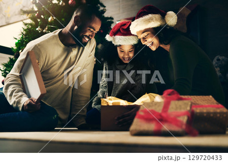 Mother, father and child with gift for Christmas in celebration of a Christian winter holiday as a happy family. Night, mom and dad love giving young girl a surprise present to celebrate xmas at home 129720433