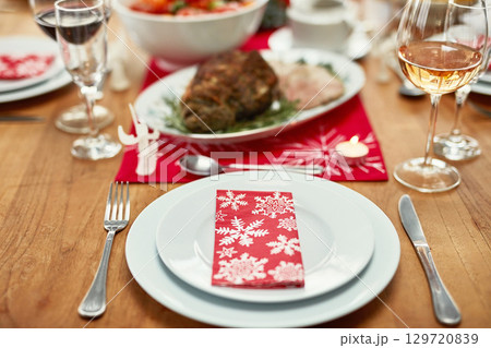 Wine glass, plate and cutlery on the table at a christmas party or event in the dining room of a house. Napkin, table setting and dinner party for a festive xmas holiday lunch celebration at a home. Wine glass, plate and cutlery on the table at a christmas party or event in the dining room of a house. Napkin, table setting and dinner party for a festive xmas holiday lunch celebration at a home. 129720839