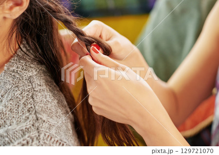 Styling, hair care and hands of friends braiding at a salon, grooming and fun together in a house. Hairstyle, stylist and girl at a hairdresser for care for hair and luxury treatment for brunette Styling, hair care and hands of friends braiding at a salon, grooming and fun together in a house. Hairstyle, stylist and girl at a hairdresser for care for hair and luxury treatment for brunette 129721070