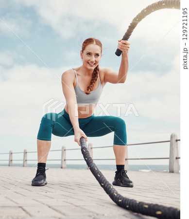 Woman, battle rope exercise and smile at ocean park for fitness, strong body and wellness at outdoor training. Girl, focus and workout by sea with goal, health or motivation for muscle development 129721195