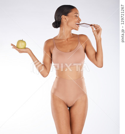 Apple, body and woman eating chocolate in a studio for a sweet snack, candy or craving. Health, wellness and female model enjoying cocoa treat while holding fruit for balance diet by gray background. 129721267