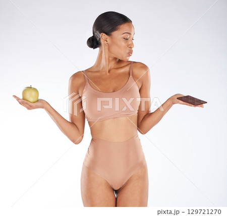 Black woman, studio and choice for chocolate, apple and health for weight loss, body or nutrition by background. Gen z model, underwear or decision for diet, fruit or candy for thinking of cheat day 129721270