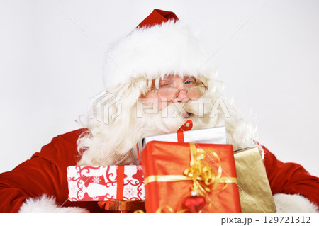Christmas, santa and gift portrait with wink for traditional festive holiday advertising. Present, giving and santa claus man with colorful ribbon boxes on white studio mockup marketing. 129721312