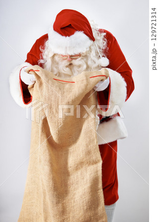 Santa Claus, bag and gift with a man in a costume posing in studio on a gray background for the holidays. Delivery, Father Christmas and sack with a male in an outfit for festive season celebration Santa Claus, bag and gift with a man in a costume posing in studio on a gray background for the holidays. Delivery, Father Christmas and sack with a male in an outfit for festive season celebration 129721314