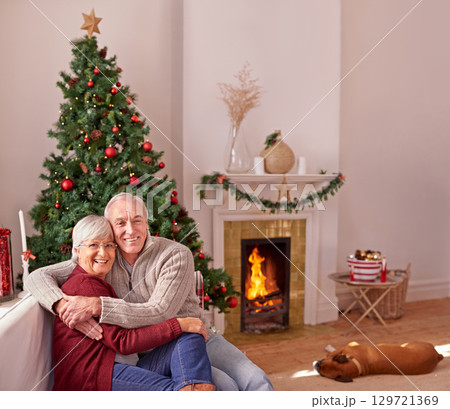 Love, senior couple on sofa and Christmas time in living room with dog at fireplace. Relax, portrait of old man and woman hugging on couch, Christmas tree, smile and retirement holiday celebration. 129721369