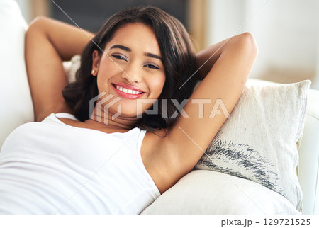 Portrait, relax and happy with a black woman lying on a sofa in the living room of her home over a weekend. Face, smile and rest with a young female chilling in a house with hands behind her head 129721525