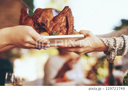 Chicken, lunch and hands at a party, celebration or Christmas event for eating together. Food, nutrition and people giving a turkey on a plate for dinner, feast and fine dining in nature with bokeh 129721749