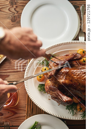 Hands, food and carving the turkey with a senior man using a knife at a dining room table in his home. Chicken, thanksgiving and tradition with a mature male cutting meat during a roast meal or feast 129721798