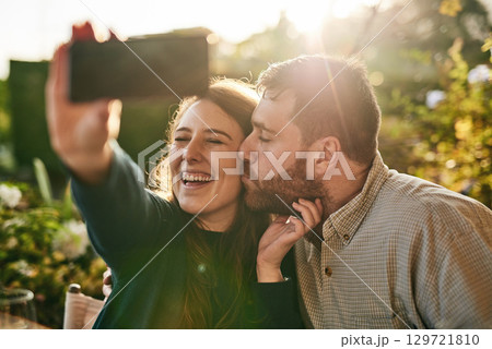 Love, couple and selfie on a patio by happy people kiss, bond and relax at sunset together. Family, phone and man kissing woman for picture while sitting in a backyard, smile and loving at home Love, couple and selfie on a patio by happy people kiss, bond and relax at sunset together. Family, phone and man kissing woman for picture while sitting in a backyard, smile and loving at home 129721810