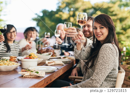 Toast, dinner and family with a group of people enjoying a meal together while drinking alcohol outdoor. Portrait, party and cheers with a female and relatives bonding in festive celebration 129721815