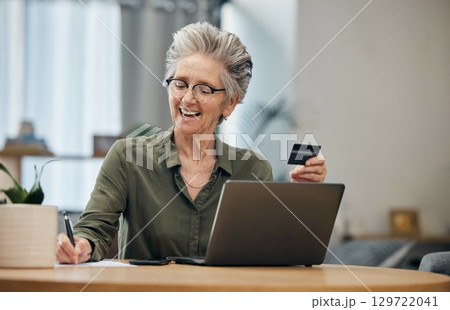 Laptop, credit card and senior woman paying her bills, debt or mortgage with online banking. Elderly lady planning a financial investment or calculating her retirement finances on paper at her home. 129722041