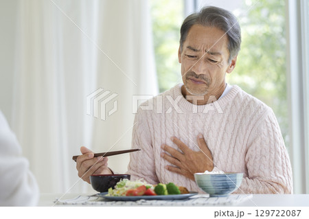 食卓で胃のあたりに手をあてるシニア男性 129722087