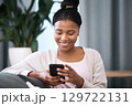 Phone, relax and happy black woman in her living room networking on social media or the internet. Happiness, smile and African girl typing a text message on smartphone while relaxing on sofa at home. 129722131