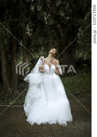 bride in white dress and long veil stands among trees. 129723906