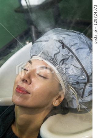 In a beauty salon, a girl client is getting her hair straightened In a beauty salon, a girl client is getting her hair straightened 129724073
