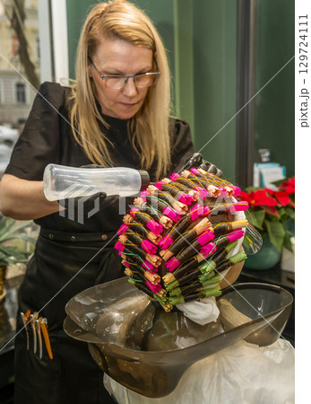 A beauty salon specialist curls a client's hair with curlers 129724111
