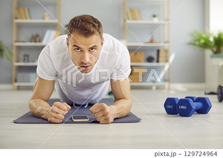 Young attractive man doing plank exercise lying on yoga mat on the floor at home. Young attractive man doing plank exercise lying on yoga mat on the floor at home. 129724964
