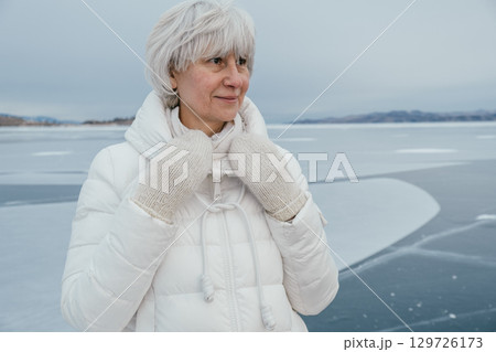 older woman enjoys winter moment on frozen lake, dressed warmly in white attire and mittens. closeup older woman enjoys winter moment on frozen lake, dressed warmly in white attire and mittens. closeup 129726173