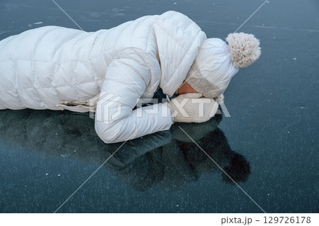 woman observes frozen surface lake while lying on ice on cold winter day. closeup. woman observes frozen surface lake while lying on ice on cold winter day. closeup. 129726178