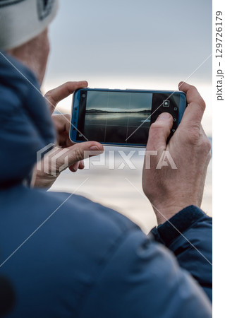 capturing serene landscape at sunrise with smartphone by lakeside in winter. closeup. capturing serene landscape at sunrise with smartphone by lakeside in winter. closeup. 129726179