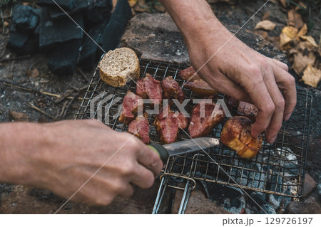 cooking meat over an open fire while camping in wooded area during autumn. closeup. 129726197