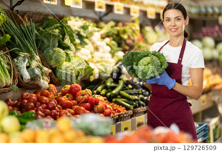 While working in shop, girl shop assistant add cabbage in showcase 129726509