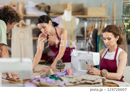 Man tailor and female dressmaker sketching dress designs on paper. Woman working on sewing machine 129726607