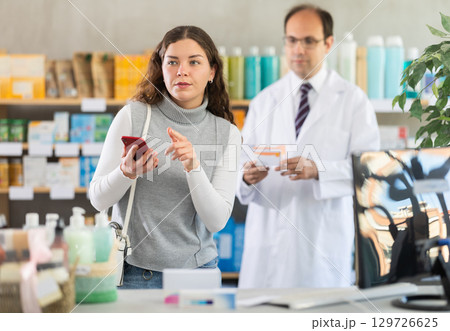 Woman with phone chooses pills with help of pharmacist 129726625