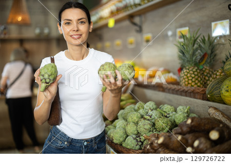 Positive woman shopping in organic food store, choosing artichokes Positive woman shopping in organic food store, choosing artichokes 129726722