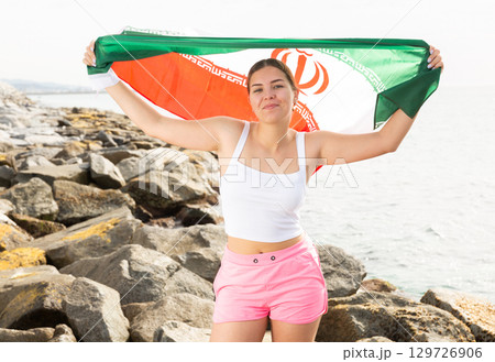 Pretty young girl holding the Iran flag in her hands on the seashore on sunny day 129726906