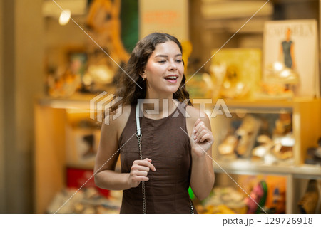 Beautiful young girl customer choosing something in souvenir shop during tourist trip in Spain Beautiful young girl customer choosing something in souvenir shop during tourist trip in Spain 129726918