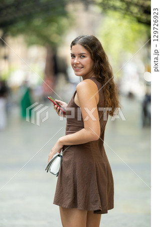 Back view of positive young woman watching smartphone walking in street of Barcelona, lifestyle technology concept 129726923