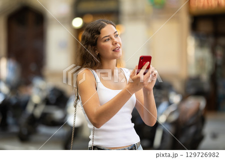 Young girl with mobile phone in her hands walking around the city and taking pictures of sights 129726982