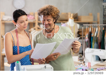 Male tailor shows paper sketch of dress to woman client, Male tailor shows paper sketch of dress to woman client, 129726989