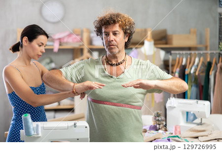 Young male tailor measuring female client in sewing workshop 129726995