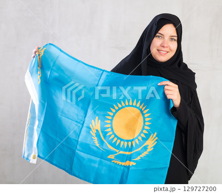 Happy young woman dressed in traditional islamic clothes with kazakh flag 129727200